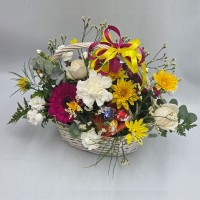 Panier fleuri avec chocolats composé de fleurs fraîches blanches, jaunes et fuchsia dans un panier tressé